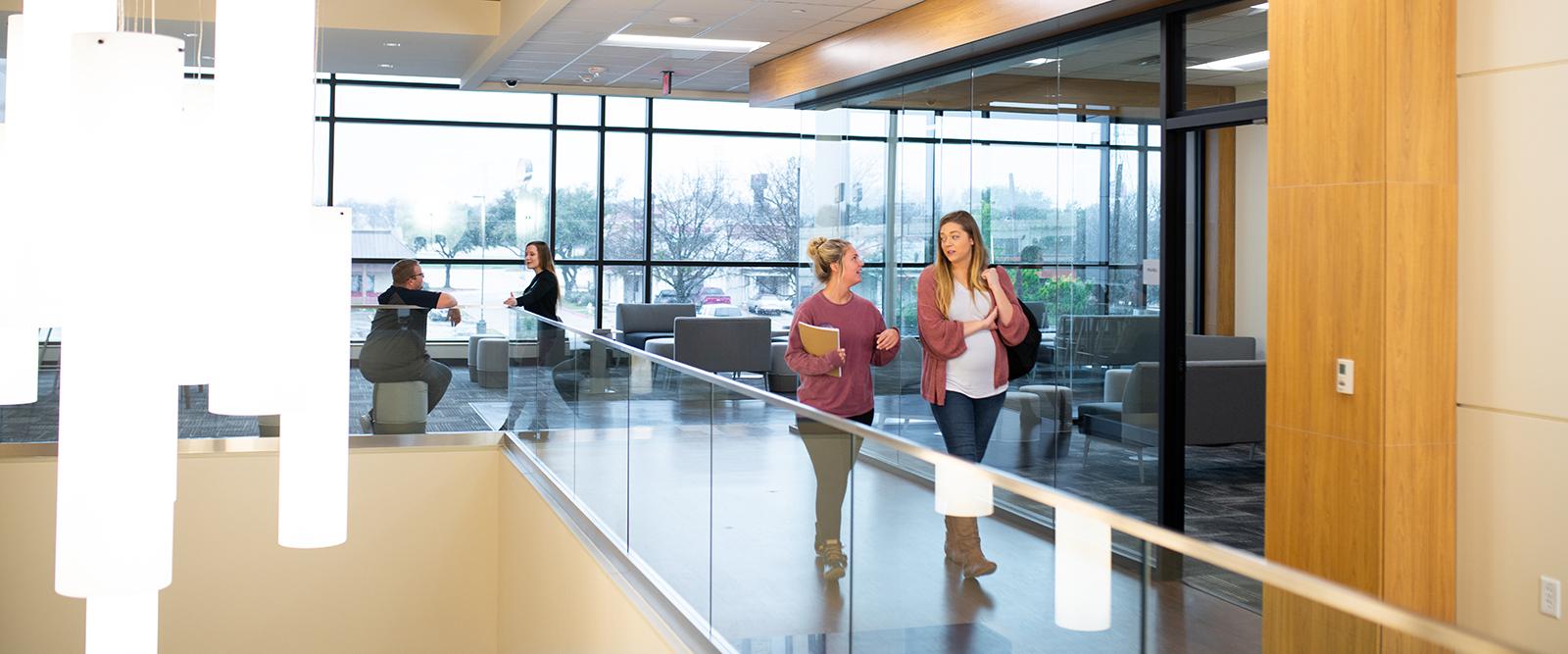 Two female students walking and talking inside the Mesquite Metroplex Center.